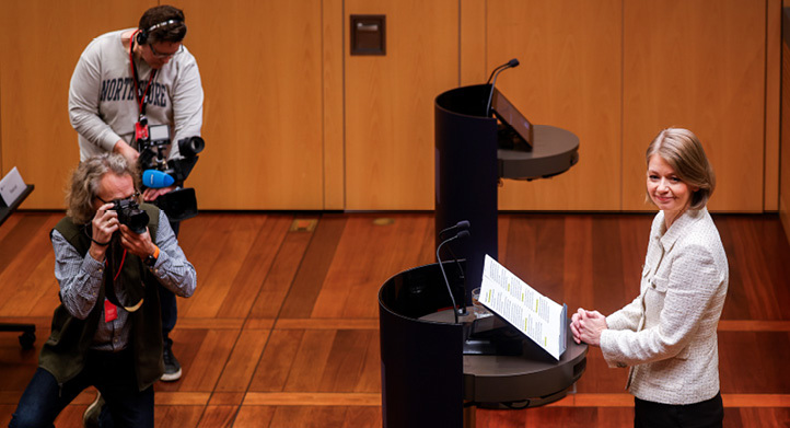 Ida Wolden Bache behind a podium with two photographers in front of her.