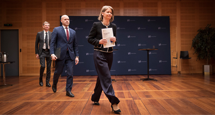 A woman and two men walk diagonally across the floor with papers in their hands