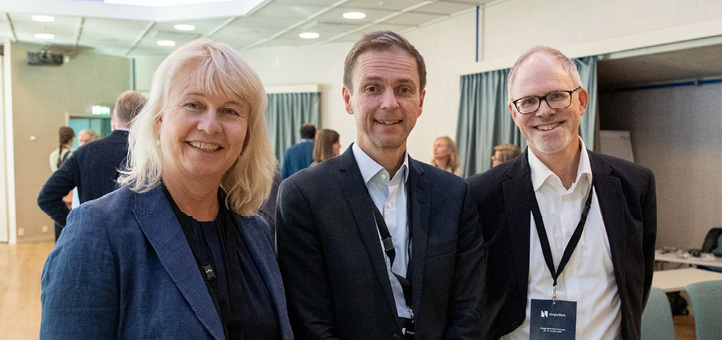 En kvinne og to menn står med akkrediteringskort rundt halsen og ser mot kamera