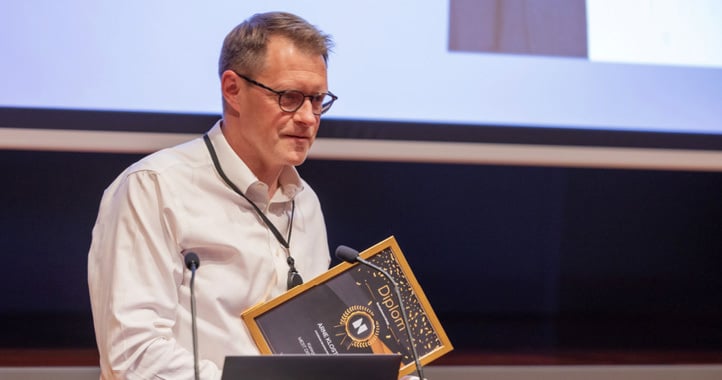 Arne Kloster at a lectern holding a diploma