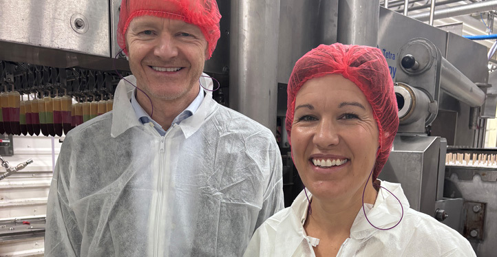 A man and woman smiling, wearing thin protective coats and hairnets, at an ice cream production plant.