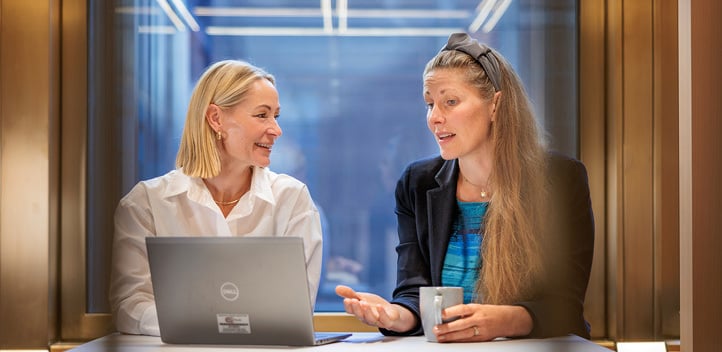 Two women sitting at a desk and having a discussion in front of an open laptop