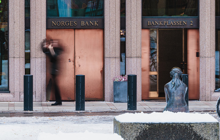 Norges Bank's double entrance doors with, in the foreground, a statue of a girl sitting down surrounded by snow