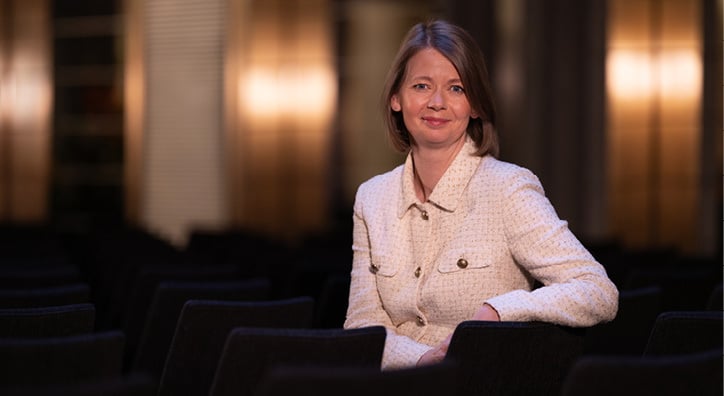 Woman sitting on a chair turning around with one arm on the back of the chair, looking towards the photographer