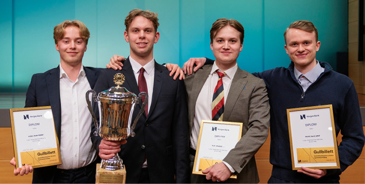 Four men who are standing and holding their diplomas and one is holding a trophy cup