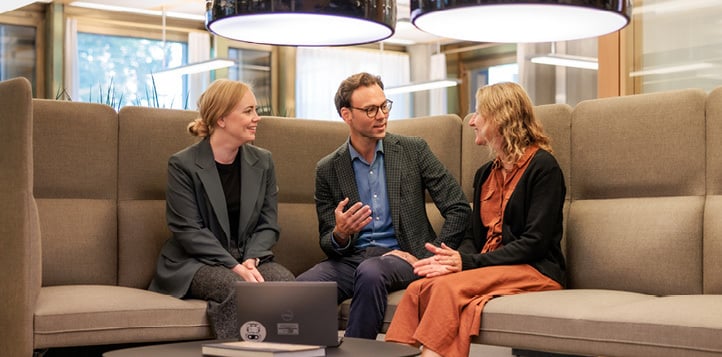 Two women and one man sitting on a sofa having a discussion