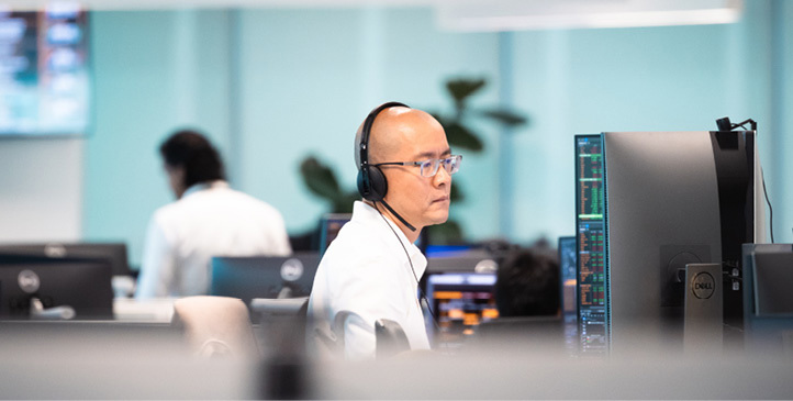Man with glasses wearing a headphone seated, looking at a computer screen