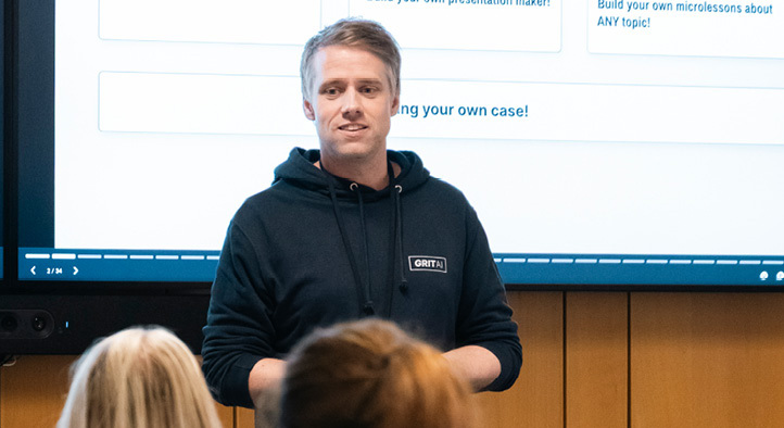 Man in hoodie giving a lecture to a group of people 