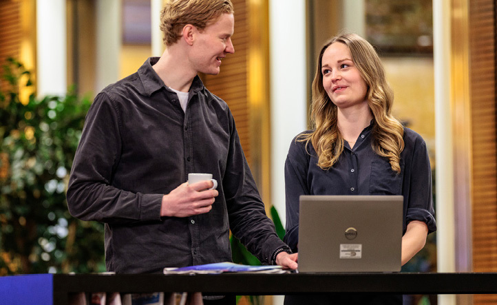 Man and woman standing and talking to each other at a table behind an open laptop computer 