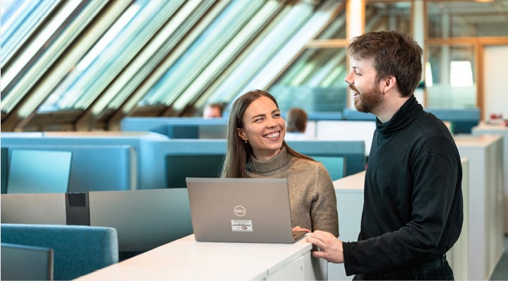 Smiling man and woman standing behind an open laptop computer 