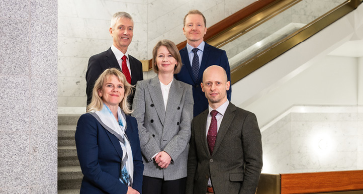 Three men and two women standing on stairway inside Norges Bank