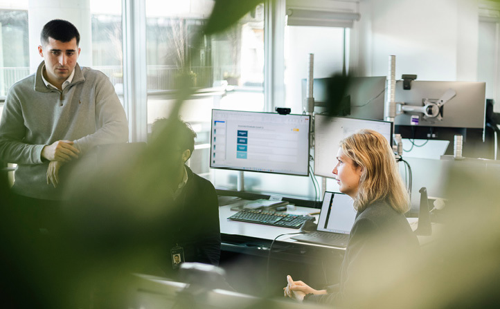 Sitting man and woman and a standing man in an office landscape, looking in the same direction 