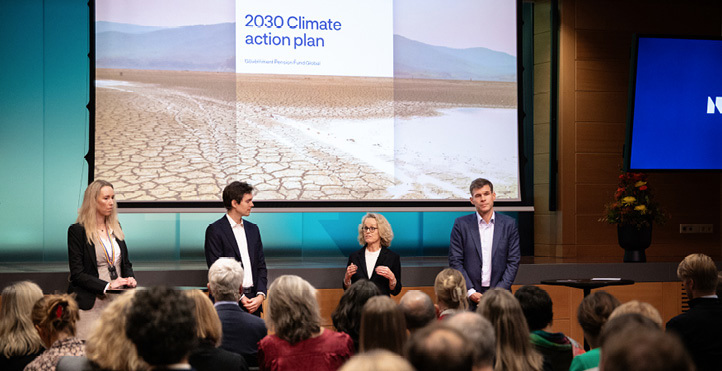 Mann og kvinne stående foran tilskuere med presentasjonsskjerm i bakgrunnen som viser et oppsprukket jord og med tittelen “2030 Climate action plan”