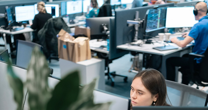 Ung kvinne i kontorlandskap sitter og ser mot skrivebordskjerm