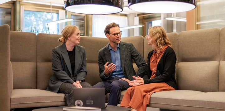 To kvinner og en mann sitter i en sofagruppe og diskuterer