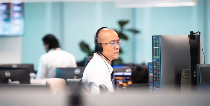 Mann med briller og hodetelefoner sitter og ser mot skrivebordskjerm