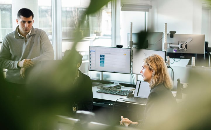 En sittende kvinne og mann og en stående mann i et kontorlandskap ser mot et felles punkt